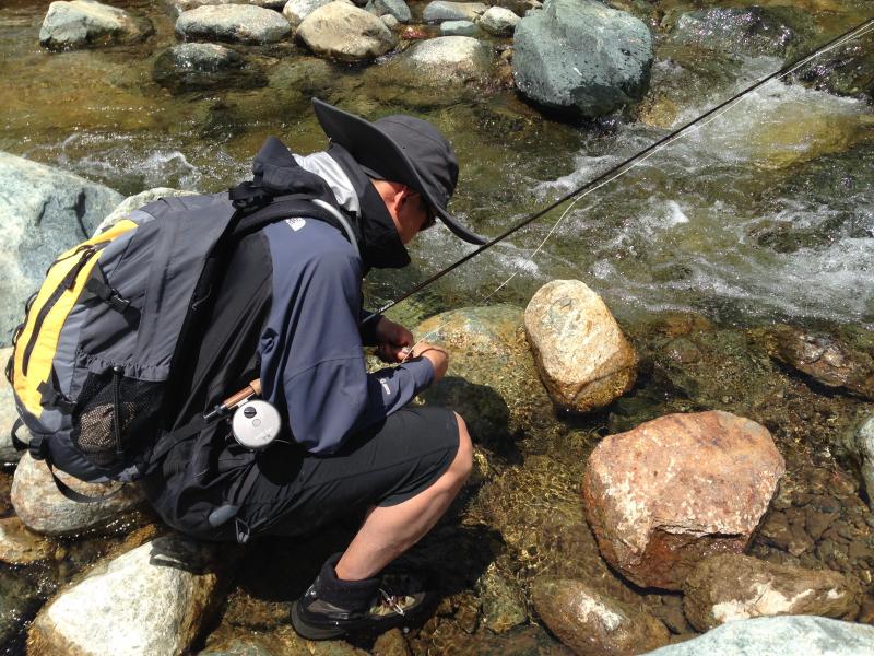 fly fisherman leaning over gear and water 